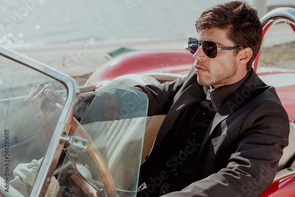 Obraz young man in convertible car looking at camera, smiling, man wears suit and tie drives red convertible car