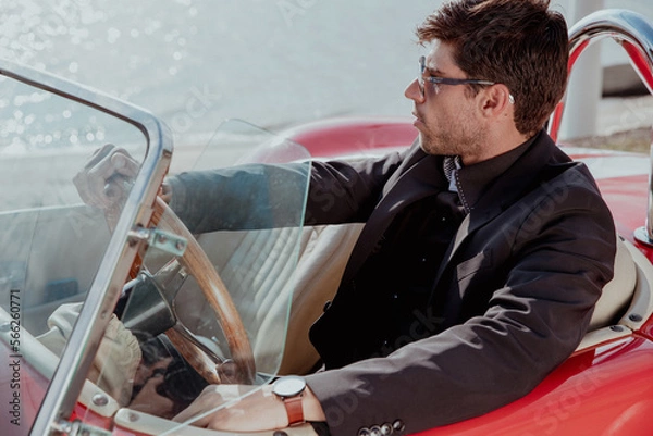 Obraz young man in convertible car looking at camera, smiling, man wears suit and tie drives red convertible car