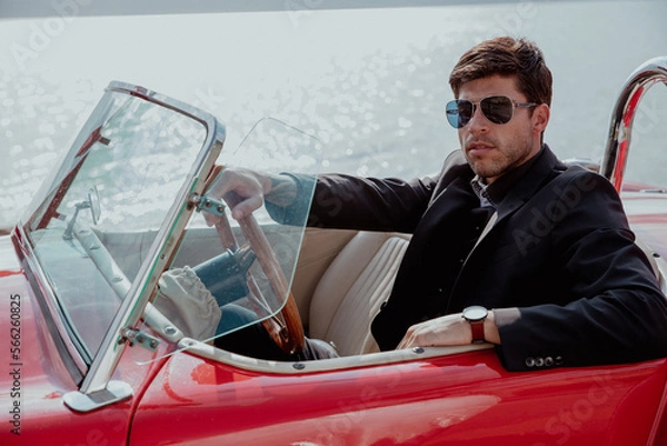 Obraz young man in convertible car looking at camera, smiling, man wears suit and tie drives red convertible car