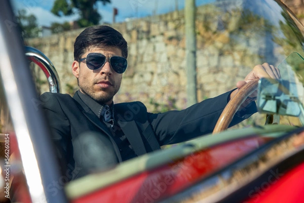 Obraz young man in convertible car looking at camera, smiling, man wears suit and tie drives red convertible car