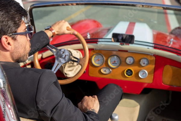 Obraz young man in convertible car looking at camera, smiling, man wears suit and tie drives red convertible car
