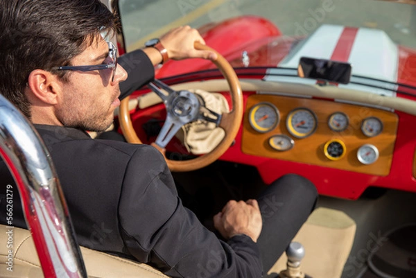 Obraz young man in convertible car looking at camera, smiling, man wears suit and tie drives red convertible car
