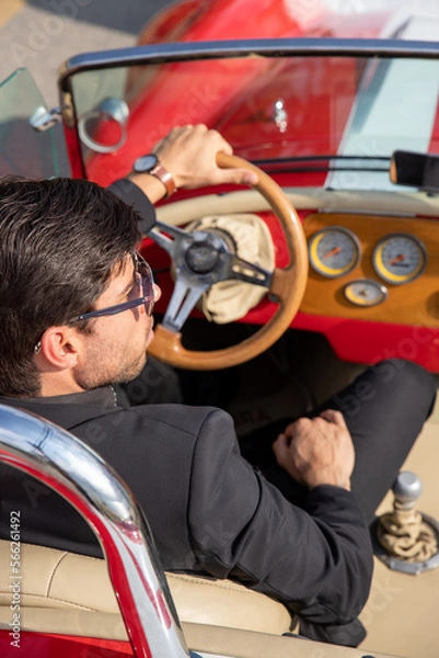 Obraz young man in convertible car looking at camera, smiling, man wears suit and tie drives red convertible carman in car