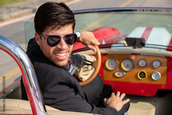 Obraz young man in convertible car looking at camera, smiling, man wears suit and tie drives red convertible car