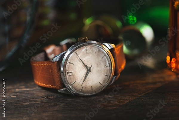 Fototapeta Vintage men's Omega dress watch with white rustic dial and brown leather strap laying on the dark brown rustic wooden table near to the instruments.