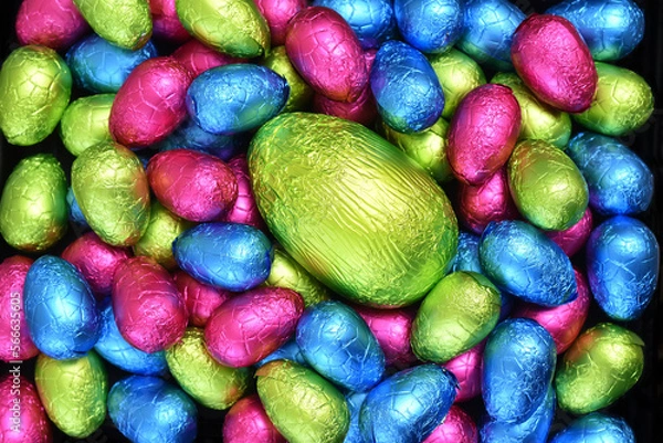 Obraz Pile or group of multi colored and different sizes of colourful foil wrapped chocolate easter eggs in pink, blue, yellow and lime green with a large green egg in the middle.