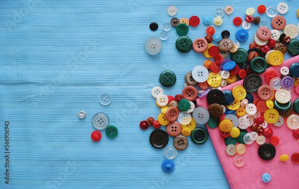 Fototapeta A lot of colored buttons for clothes on a blue fabric. Tailoring
