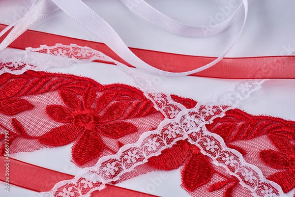 Fototapeta Various red and white lace and satin ribbons lie on a white table, close-up.