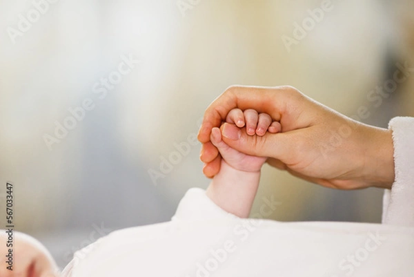 Fototapeta Close up mother holding tiny hand of little newborn baby boy girl, helping hands, bonding different generations. Happy motherhood concept.