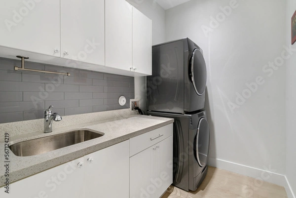 Obraz Laundry room with quarts counter top, sink, stacked washer and dryer.