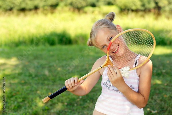 Obraz European blonde girl with badminton racket smiles cheerfully. Summer vacation concept. Children in the summer.
