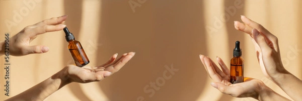 Obraz Two pairs of female hands hold amber glass vials with cosmetic serum on light brown background, in rays of sunlight. Close-up, banner. Branding, mockup concept