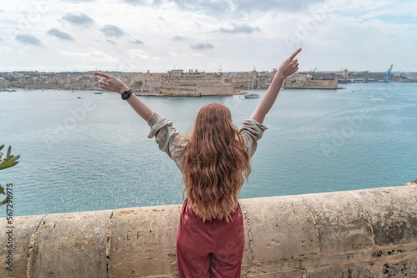 Fototapeta woman standin at a wall looking at a panoramic view of the three cities in valletta