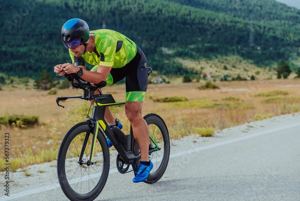 Fototapeta Full length portrait of an active triathlete in sportswear and with a protective helmet riding a bicycle. Selective focus 