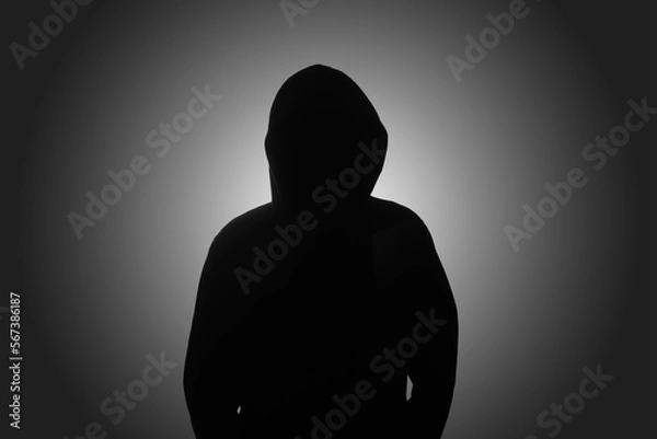 Fototapeta Mysterious man wearing black hoodie standing against dark background. Hacker, crime, and cyber security concept.