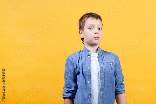 Fototapeta A portrait of a boy showing emotion of astonishment. He is surprised and looks at camera. Yellow background. Front view. Copy space