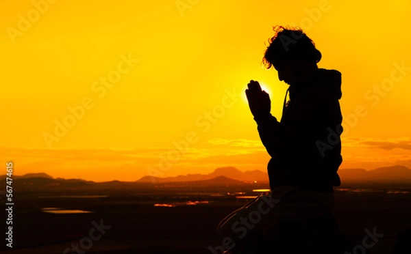 Obraz Silhouette of a male praying on top of a mountain at sunset with the sun just behind his hands. Concept of spiritualism and religion. Copy space on the right