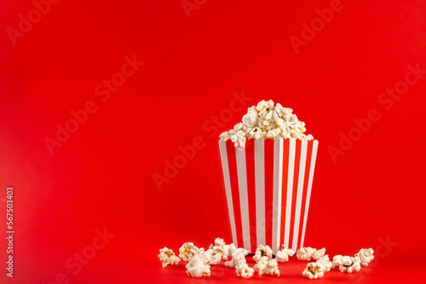 Obraz Popcorn in a red and white striped bag on a red background. Front view, copy space.