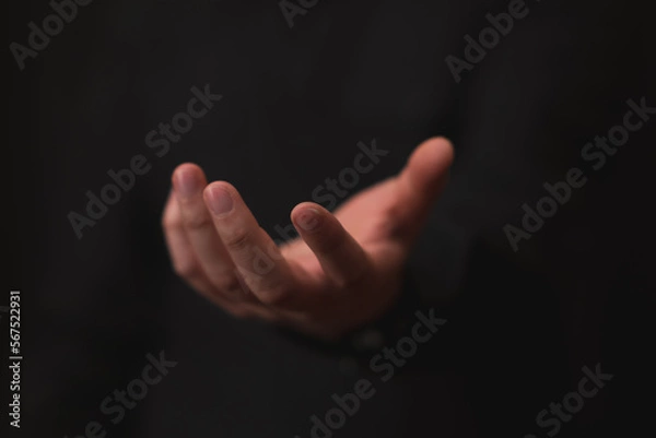 Fototapeta hand outstretched in gesture of giving or receiving, black background