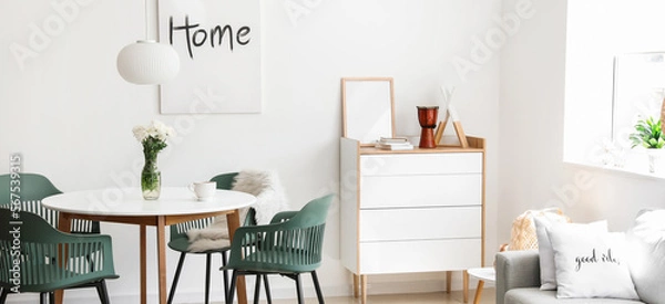 Fototapeta Stylish interior of light dining room with table, chest of drawers and sofa