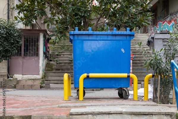 Fototapeta A blue trash can behind a yellow railing.