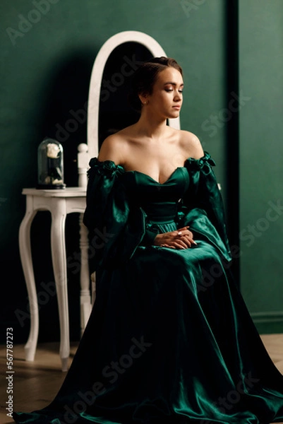 Fototapeta a girl in a green dress sitting against the background of a wall and a mirror