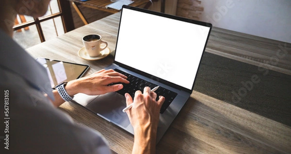 Fototapeta Businessman working on his laptop with a stylus in hand, tablet and cup of coffee. Young entrepreneur working remotely on his computer white screen mockup