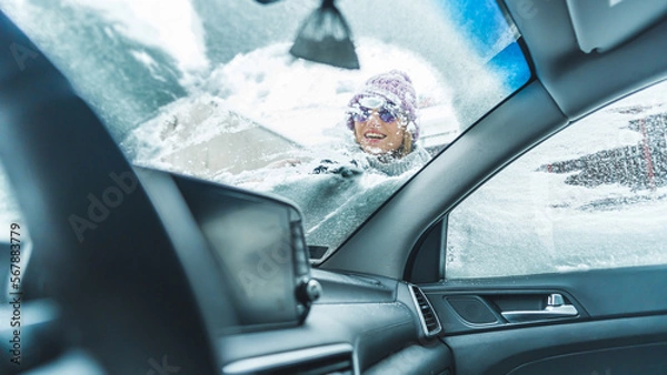 Fototapeta Smiling woman in sunglasses scraping snow off a front car window. High quality photo