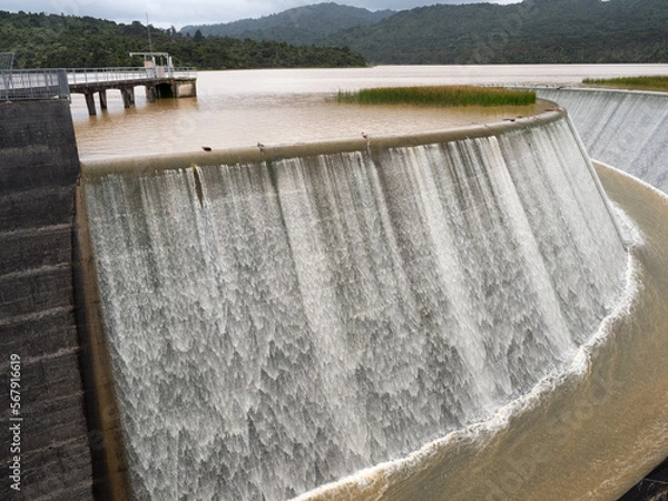 Fototapeta The Lower Nihotupu Reservoir shows water cascading and overflowing the side walls due to record breaking heavy rainfall in New Zealand.Waitakere