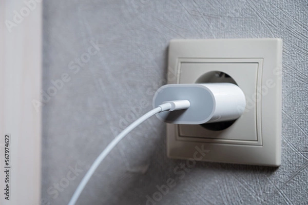 Fototapeta Horizontal photo. Phone charger in an electrical socket on the wall, close-up
