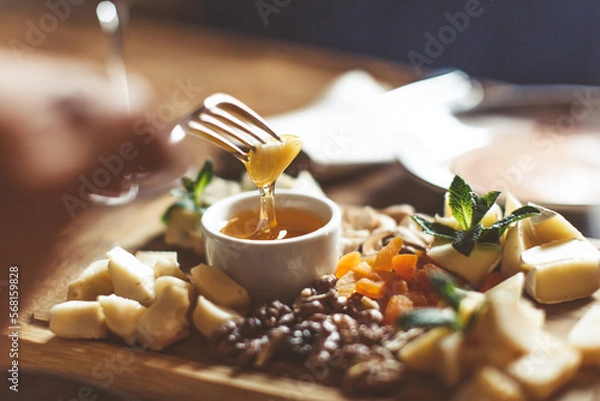 Obraz Cheese platter with different cheeses, nuts, honey, on rustic wooden background. Retro styled cheese variety selection on light wood board. High quality photo