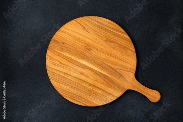Fototapeta Round empty wooden charcuterie serving board with handle on old black concrete background, shabby table. Top view. Food template, copy space. Flat lay design, mockup. Layout, cooking concept, frame.