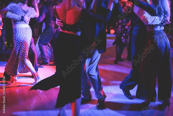 Fototapeta Couples dancing traditional latin argentinian dance milonga in the ballroom on a festival, tango studio, salsa, bachata and kizomba lesson in the red and purple lights, rehearsal in the dance class
