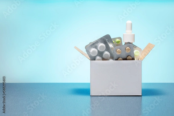 Obraz Cardboard box with different medicine pills, tablets and capsules on a blue background with copy space. Buying drug delivery concept.