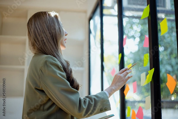 Fototapeta Team of asian business woman working with paper note on glass wall, Business people meeting to share idea at office, Business planning and Sticky note on glass wall.