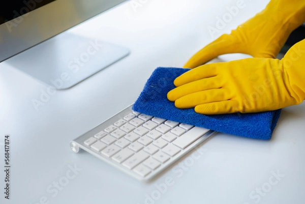 Fototapeta Person cleaning room, cleaning worker is using cloth to wipe computer keyboard in company office room. Cleaning staff. Concept of cleanliness in the organization.