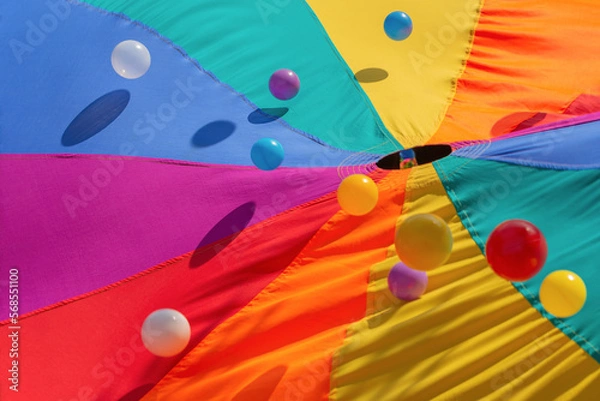 Fototapeta Multicolor-patterned kids play parachute with colorful bouncing balls. Rainbow colors toys for outdoor activities