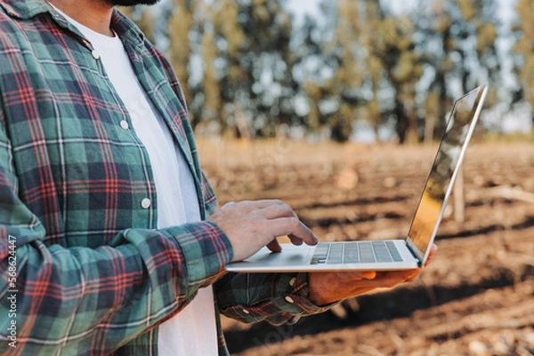 Fototapeta Close up unrecognizable farmer man teleworking on his computer in the middle of his farmland.