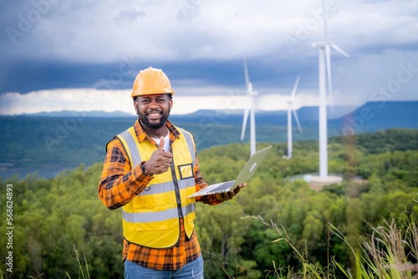 Fototapeta Portrait of engineer African American man working with laptop in wind turbine farm.