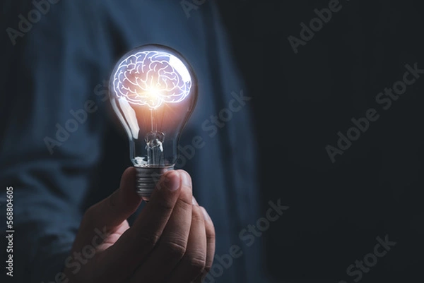Obraz businessman Hand holding light bulb with brain glowing with orange light line and ray. Creative and new business knowledge thinking idea concept.