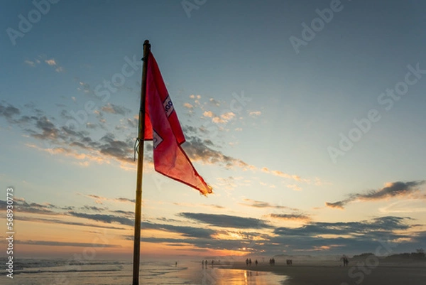 Fototapeta Red flag by the sea with sunset background.