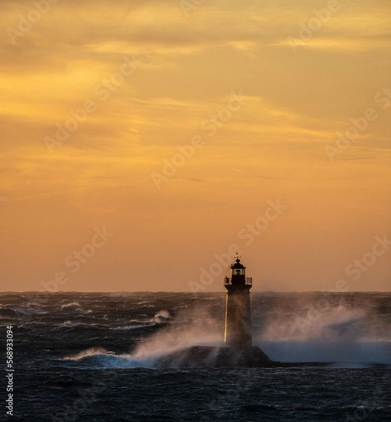 Fototapeta sunset over the sea, in the foreground a lighthouse, where the big waves a crashing into the solid build of the lighthouse 