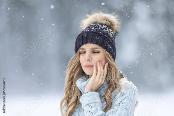 Fototapeta A young woman has a toothache outside in winter weather, she has sensitive enamel to the cold