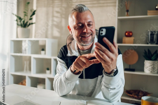 Obraz Middle aged man talking on a smartphone while working in a home office