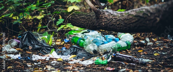 Fototapeta Garbage pile in forest among plants. Toxic plastic into nature everywhere. Rubbish heap in park among vegetation. Contaminated soil. Environmental pollution. Ecological issue. Throw trash anywhere.