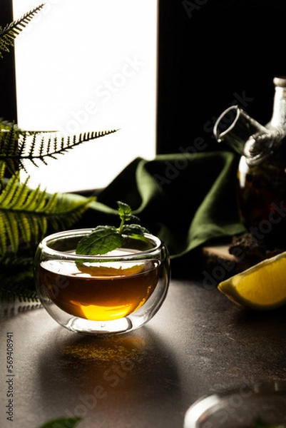 Fototapeta A glass mug with tea in the light is on the table. Custard tea with lemon. On the background of the window