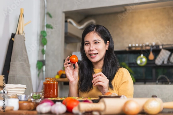 Obraz Young attractive Asian woman talking communicating during online live streaming how to cook homemade pizza indoor kitchen. content creator using camera recording food product review.