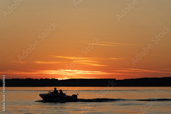 Fototapeta Silhouette of two fisherman on the boat. Beautiful sunset on the background.