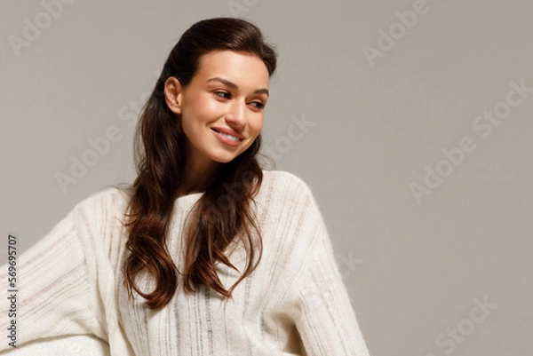 Fototapeta Happy young woman sitting on sofa at home and looking at camera. Portrait of comfortable woman in winter clothes relaxing on armchair. Portrait of beautiful girl smiling and relaxing during autumn.