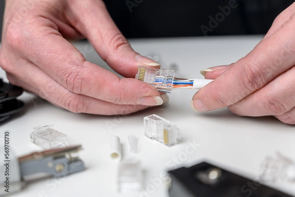 Obraz A woman's hand inserts an internet cable into a clamp connector. utp ethernet network cable plug. The concept of internet communications.